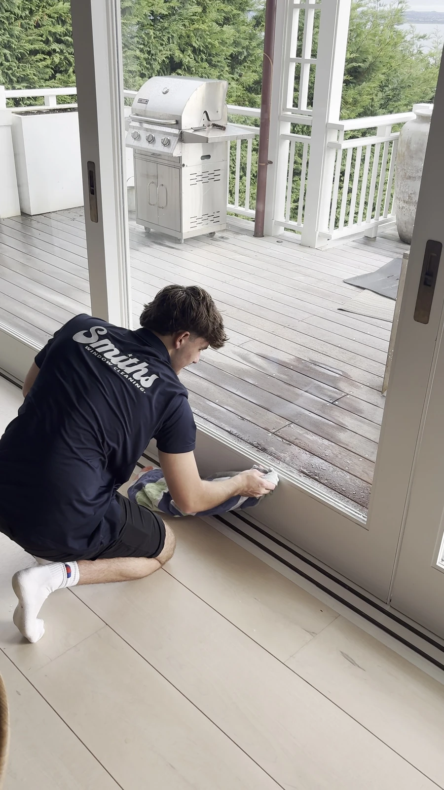 Smiths Window Cleaning technician wiping down a window frame and track on a bifold door