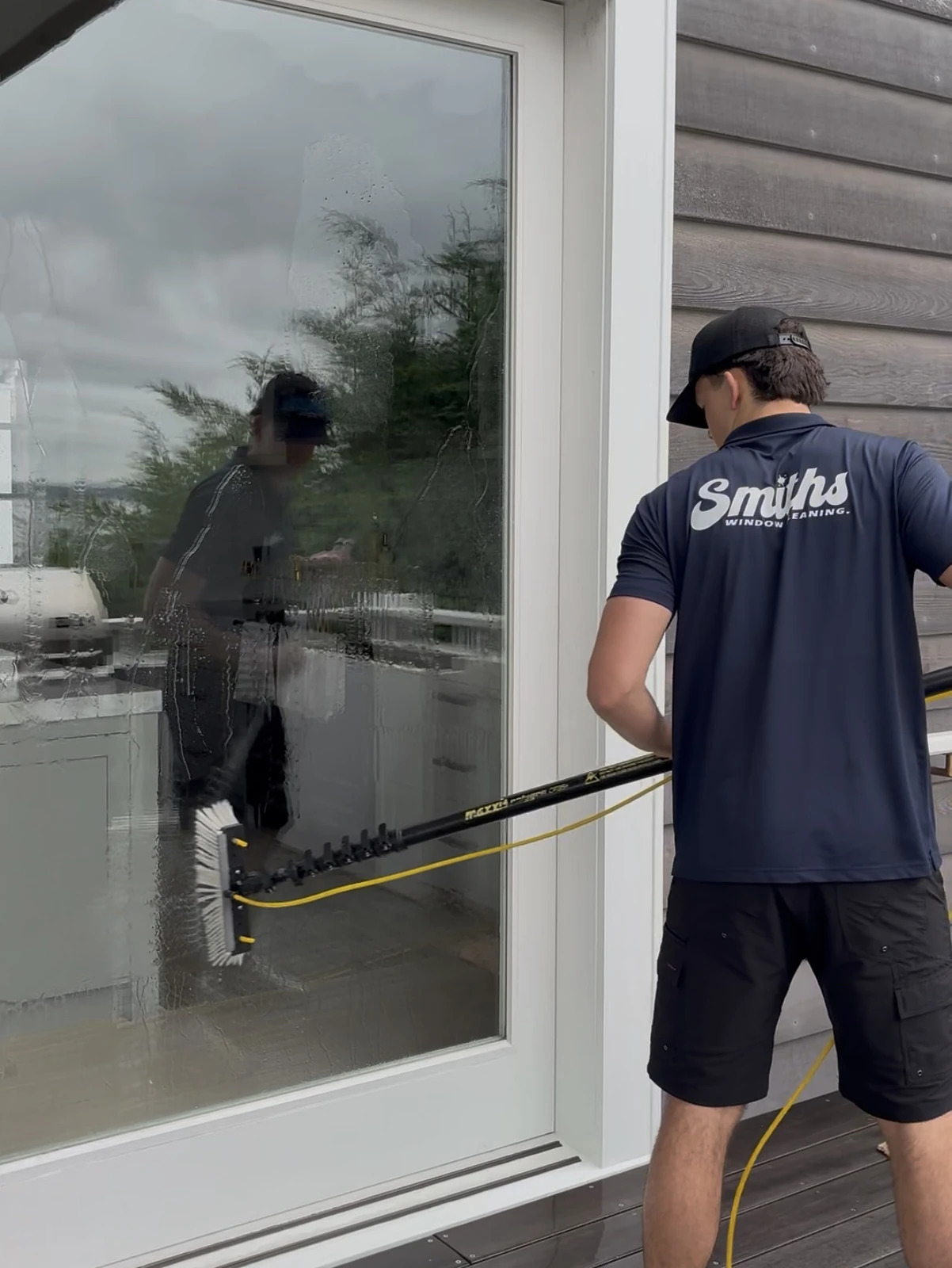 Smiths Window Cleaning technician using a water fed pole to clean a glass door on an Auckland deck